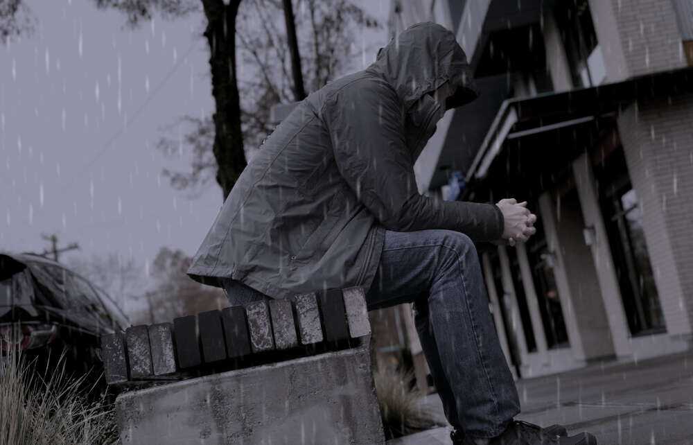 Person sitting on a bench in the rain looking dejected