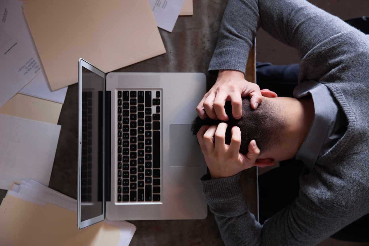 Overhead shot of a man with his head on a desk in front of his laptop, hands in his hair, apparently frustrated